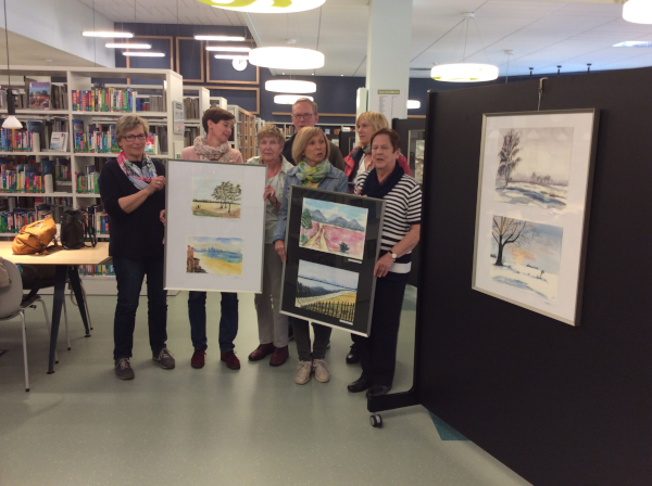 Kursteilnehmerinnen und - teilnehmer präsentieren mit Heike Wirtz, der Leiterin des VHS-Kurses Aquarellmalerei, ihre Bilder-Ausstellung in der Mediathek